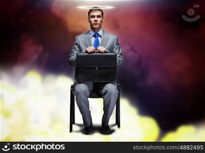 Saint businessman. Young businessman with halo above head sitting on chair