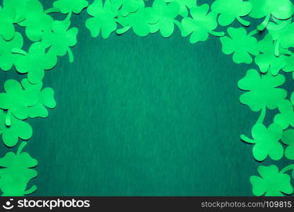 Saint Patrick banner concept with a bunch of green paper clovers displayed in an arch, on a dark green wooden background with space for text.