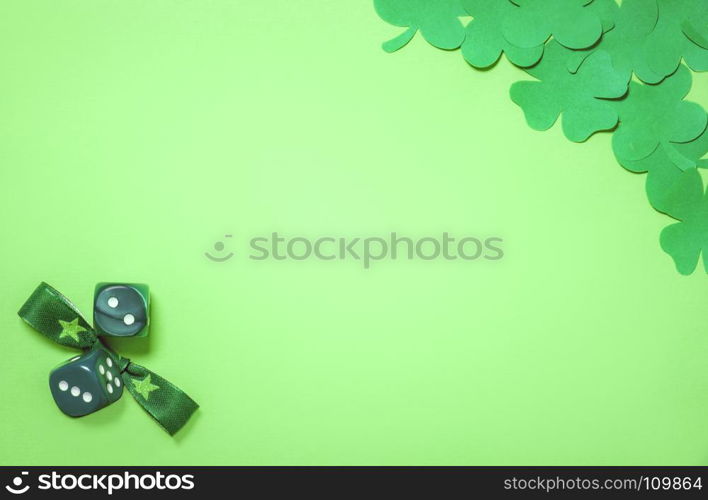 Saint Patrick concept with dark green paper clovers in a corner and a bow tie and dices in the other, placed on a blank light green paper sheet.