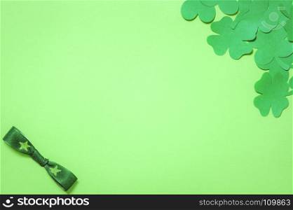 Saint Patrick frame design, with a bunch of paper clovers in a corner and a bow tie in the other, displayed on a blank green paper background.