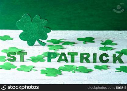Saint Patrick words spelled with green wooden letters and a big green shamrock in the back, surrounded by paper clovers, on a wooden background.