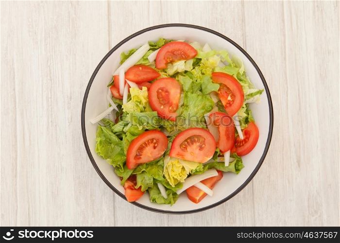 Salad bowl with lettuce tomato and onion on a white wooden background