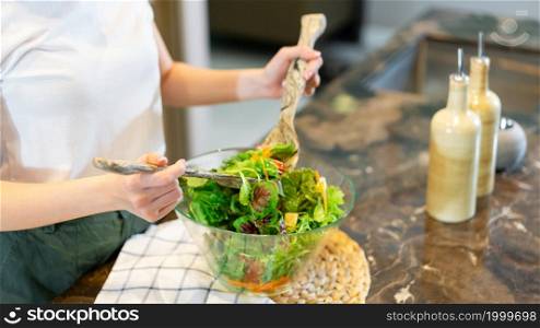 salad concept the woman with white t-shirt and dark green pants standing at the kitchen and making a bowl of green salad.