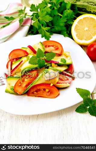 Salad from a young zucchini, radish, tomato and mint, seasoned with lemon juice and soy sauce in a white plate, a napkin on the background of a light wooden board