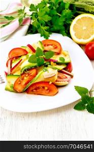 Salad from a young zucchini, radish, tomato and mint, seasoned with lemon juice and soy sauce in a white plate, a napkin on the background of a light wooden board