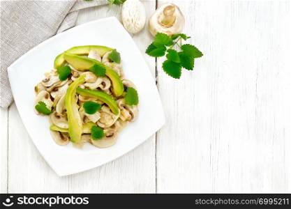 Salad from avocado and raw champignons, seasoned with lemon juice and vegetable oil with mint leaves, towel against the background of a wooden board on top