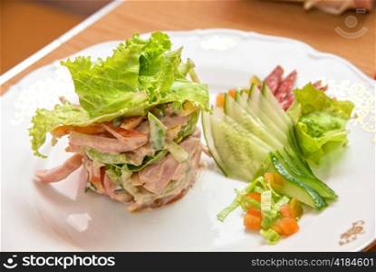 Salad from different kinds of sausages, cucumbers, peppers, lettuce with sour cream sauce