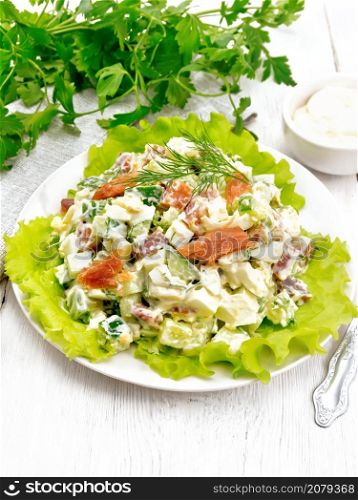 Salad from salmon, cucumber, eggs and avocado, dressed with mayonnaise on lettuce leaves in a plate, napkin, dill, parsley and fork on a light wooden board background