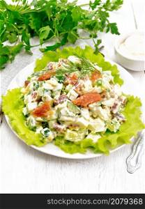 Salad from salmon, cucumber, eggs and avocado, dressed with mayonnaise on lettuce leaves in a plate, napkin, dill, parsley and fork on a light wooden board background