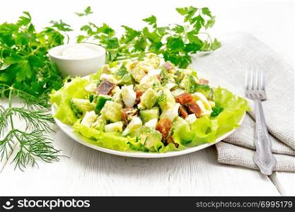 Salad from salmon, cucumber, eggs and avocado with mayonnaise on lettuce leaves in a plate, kitchen towel, dill, parsley and fork on a wooden board background
