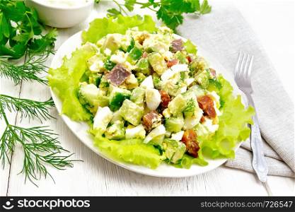 Salad from salmon, cucumber, eggs and avocado with mayonnaise on lettuce leaves in a plate, kitchen towel, dill, parsley and fork on a light wooden board background