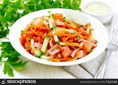 Salad from smoked sausage, spicy carrot, tomato, cucumber and spices with mayonnaise, towel, fork and parsley on a light wooden board background