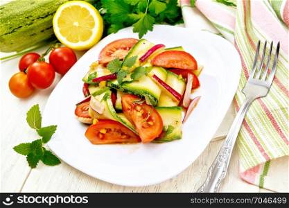 Salad from young zucchini, radish, tomato and mint flavored with lemon juice and soy sauce in a white plate, napkin and fork on a wooden plank background