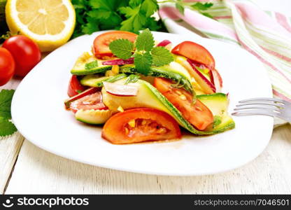 Salad from young zucchini, radish, tomato and mint flavored with lemon juice and soy sauce in a plate, napkin on a light wooden board background