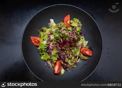 salad in a black plate, on a black wooden background