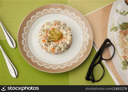 salad in a plate with book and glasses and cutlery on a green tablecloth. Breakfast and a book on a green tablecloth