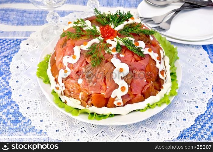Salad layered with salmon, egg, crab meat and rice, mayonnaise in a plate on a green lettuce on the background of a blue tablecloth
