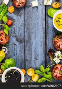 Salad making, food frame with oil,vinegar, tomatoes, basil and cheese on blue rustic wooden background, top view, vertical