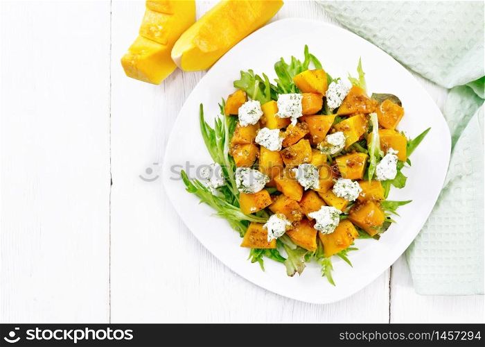 Salad of baked pumpkin, arugula with balls of salt cheese, seasoned with honey, grainy mustard, garlic and vegetable oil in a plate, napkin and fork on wooden board background from above