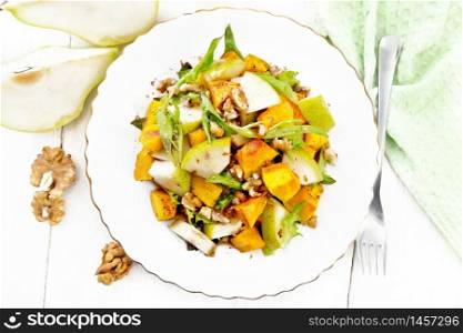 Salad of baked pumpkin, fresh pear, arugula and walnuts, seasoned with honey, balsamic vinegar, spices and vegetable oil in a plate on wooden board background from above