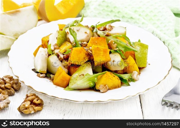 Salad of baked pumpkin, fresh pear, arugula and walnuts, seasoned with honey, balsamic vinegar, spices and vegetable oil in plate on a wooden board background