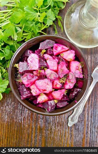 Salad of beets and potatoes, seasoned with vegetable oil and vinegar in a bowl, parsley and a fork on the background of a dark wooden board on top