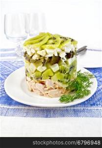 Salad of chicken, boiled potatoes, eggs, pickled cucumber and kiwi in a plate on a background of a linen tablecloth