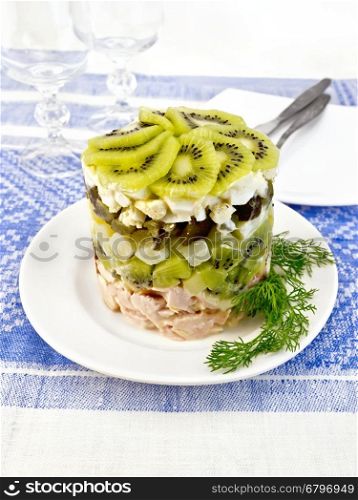 Salad of chicken, boiled potatoes, eggs, pickled cucumber and kiwi in a plate on a background of blue linen tablecloth