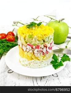 Salad of crab meat, cheese, eggs and green apple in the plate, napkin, dill on the background light wooden boards