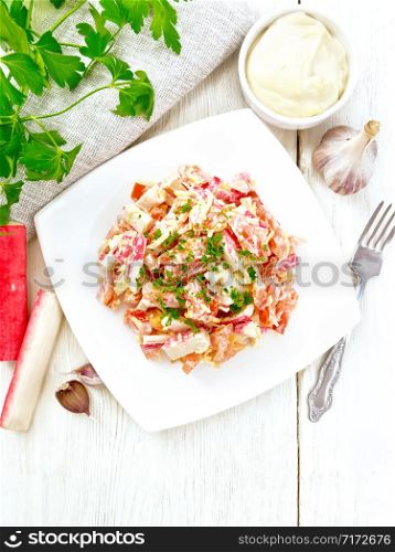 Salad of crab sticks, cheese, garlic and tomatoes, dressed with mayonnaise, towel and parsley on a wooden board background from above