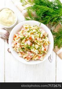 Salad of crab sticks, cheese, garlic, eggs and tomatoes, dressed with mayonnaise in a plate, kitchen towel and parsley on a wooden board background from above