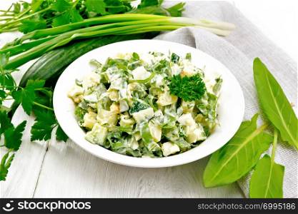 Salad of cucumber, sorrel, boiled potatoes, eggs and herbs, dressed with mayonnaise in a white plate, parsley, green onions and towel against the background of light wooden boards