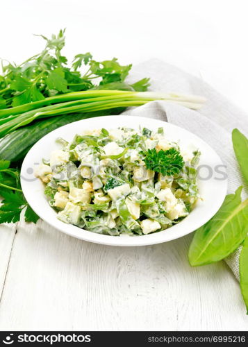 Salad of cucumber, sorrel, boiled potatoes, eggs and herbs, dressed with mayonnaise in a white plate, parsley, green onions and kitchen towel on wooden board background