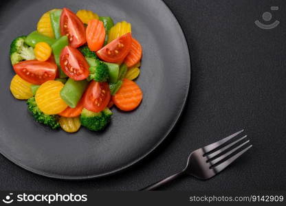 Salad of fresh and steamed vegetables cherry tomatoes, broccoli, carrots and asparagus beans on a dark concrete background