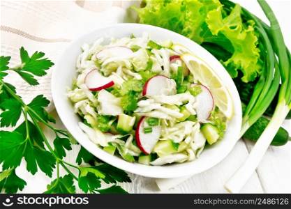 Salad of fresh cabbage, radish, lettuce, cucumber and green onion dressed with vegetable oil in plate, towel and parsley on white wooden board background