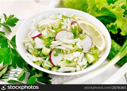 Salad of fresh cabbage, radish, lettuce, cucumber and green onion salad dressed with vegetable oil in a plate, napkin and parsley on white wooden board background
