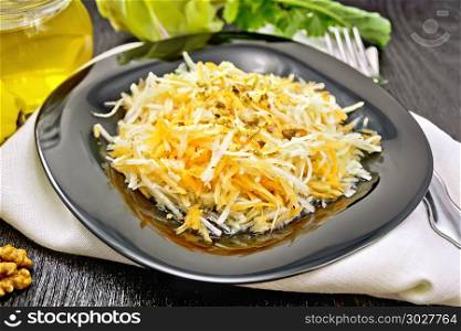 Salad of fresh carrots, kohlrabi cabbage and walnuts, seasoned with honey and lemon juice in a plate on a napkin on a dark wooden board background. Salad of carrot and kohlrabi with honey in plate on black board