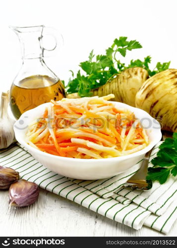 Salad of fresh carrots, parsnip and garlic with vegetable oil in a plate on a napkin, fork, parsley and root vegetables on wooden board background