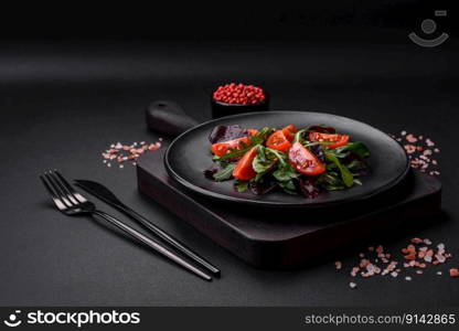 Salad of fresh cherry tomatoes, arugula, spinach, young beet leaves and other greens on a dark concrete background