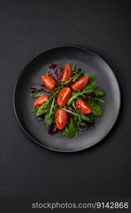 Salad of fresh cherry tomatoes, arugula, spinach, young beet leaves and other greens on a dark concrete background