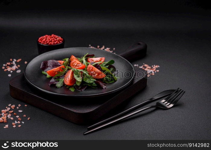 Salad of fresh cherry tomatoes, arugula, spinach, young beet leaves and other greens on a dark concrete background