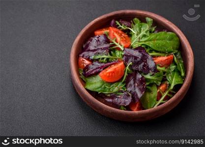 Salad of fresh cherry tomatoes, arugula, spinach, young beet leaves and other greens on a dark concrete background