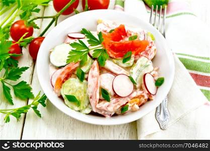 Salad of fresh tomatoes, cucumbers and radish with green onions and parsley, flavored with mayonnaise and sour cream in a plate, towel and fork on the background of a light wooden board