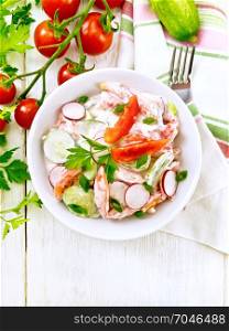 Salad of fresh tomatoes, cucumbers and radish with green onions and parsley, flavored with mayonnaise and sour cream in a bowl, towel and fork on the background of a light wooden board on top