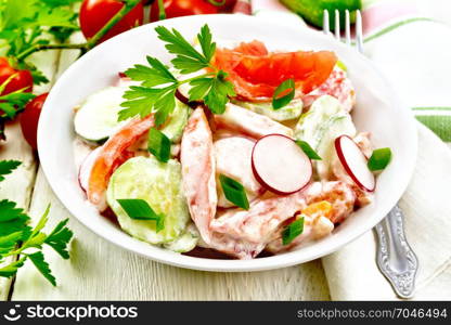 Salad of fresh tomatoes, cucumbers and radish with green onions and parsley, flavored with mayonnaise and sour cream in a plate, napkin and fork on the background of a light wooden board