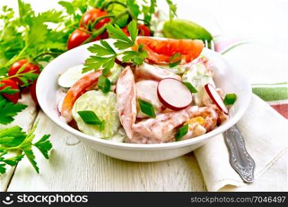 Salad of fresh tomatoes, cucumbers and radish with green onions and parsley, flavored with mayonnaise and sour cream in a bowl, towel and fork on a wooden plank background