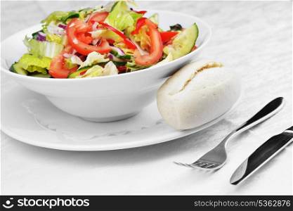 salad of fresh vegetable with bun on white dish.