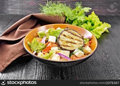 Salad of fried eggplant, fresh tomato, lattuk with red onion and salted feta cheese, seasoned with vegetable oil and soy sauce in a plate, napkin and parsley on wooden board background
