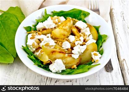 Salad of fried pear, spinach, salted feta cheese and cedar nuts in a plate, napkin on a light wooden board background