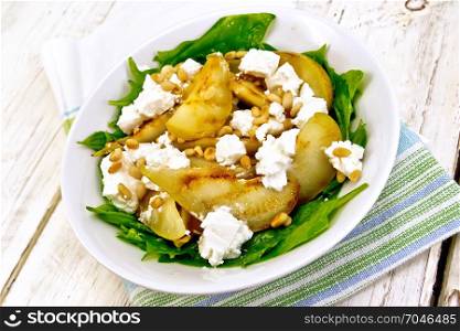 Salad of fried pear, spinach, salted feta cheese and cedar nuts in a plate on a napkin on a light wooden board background